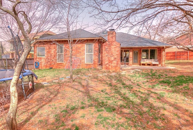 rear view of property featuring a patio, a trampoline, fence, brick siding, and a chimney