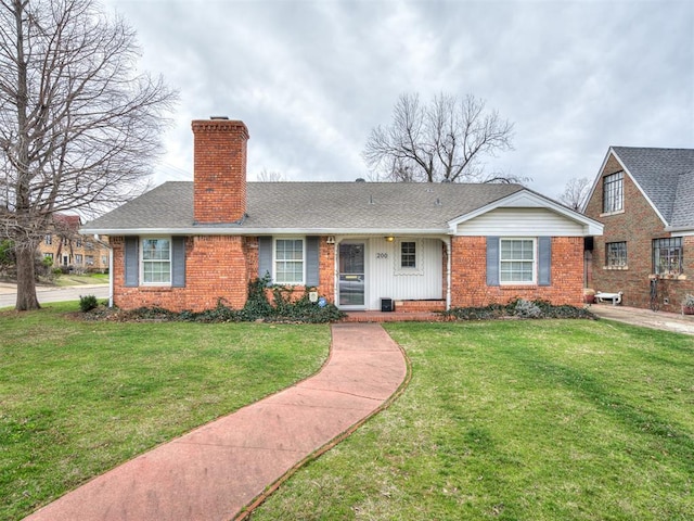 view of front of house featuring a shingled roof, a front yard, brick siding, and a chimney