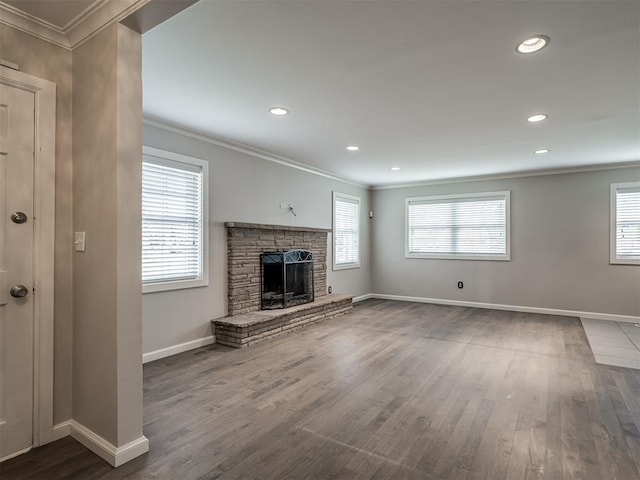 unfurnished living room featuring a wealth of natural light, a stone fireplace, dark wood-style flooring, and crown molding