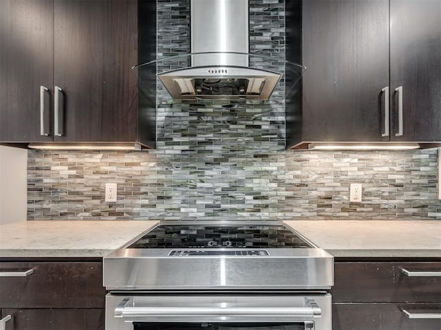 kitchen featuring stainless steel electric range oven, dark brown cabinets, wall chimney exhaust hood, and decorative backsplash