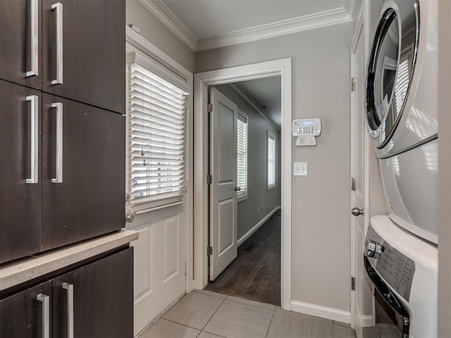 washroom with ornamental molding, cabinet space, baseboards, and stacked washing maching and dryer