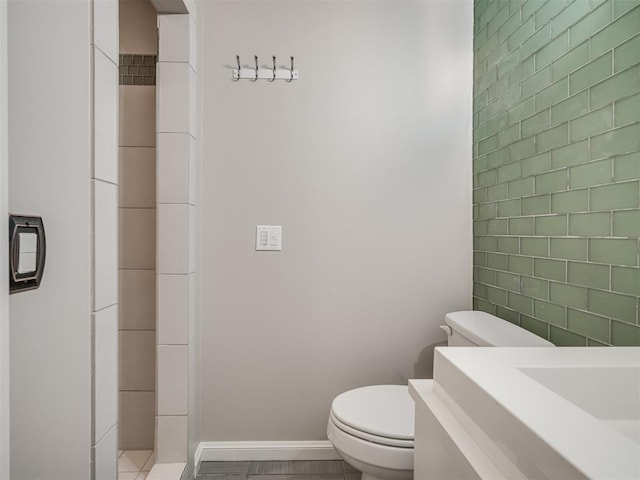 bathroom featuring tile walls, toilet, and baseboards