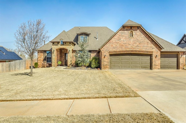 2241 W Mickey Dr, Mustang, OK 73064 - french country home with fence, driveway, brick siding, and roof with shingles