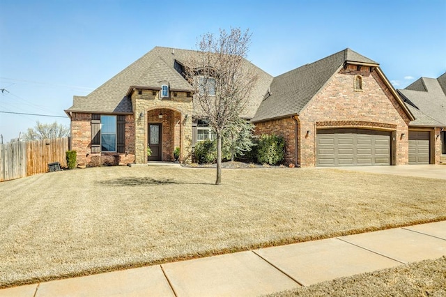 2241 W Mickey Dr, Mustang, OK 73064 - french country home with fence, concrete driveway, brick siding, a front yard, and a garage