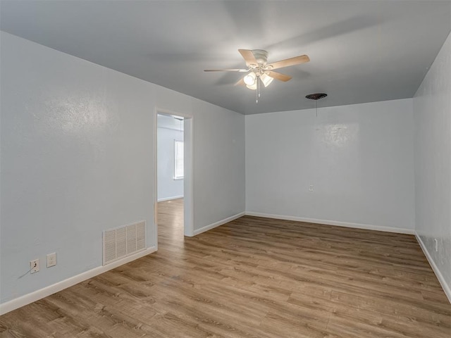 empty room with a ceiling fan, wood finished floors, visible vents, and baseboards