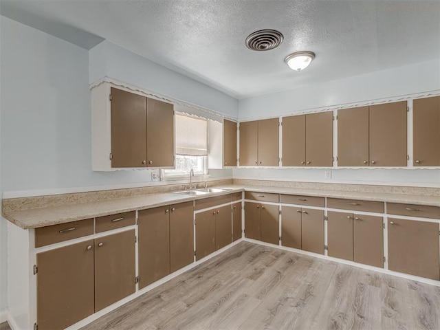 kitchen with light wood finished floors, visible vents, a textured ceiling, and a sink