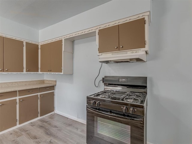 kitchen with baseboards, under cabinet range hood, light countertops, light wood-type flooring, and gas stove