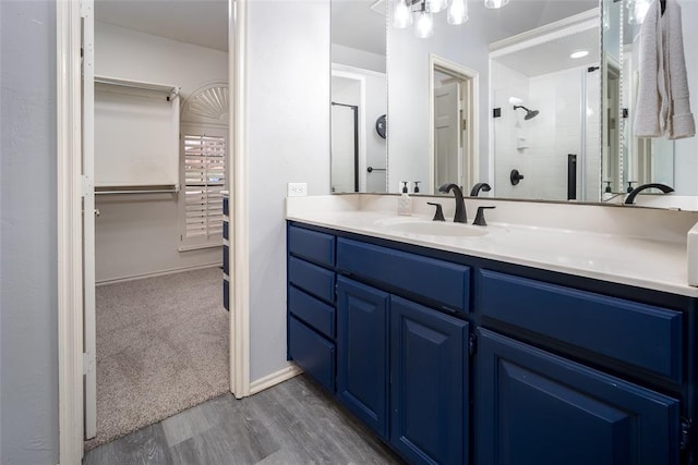 full bathroom with a spacious closet, a shower stall, baseboards, wood finished floors, and vanity