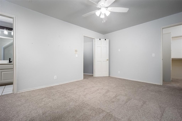 unfurnished bedroom with a spacious closet, baseboards, carpet flooring, ensuite bathroom, and a ceiling fan