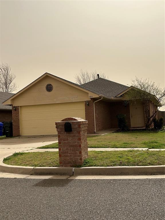 ranch-style house featuring a front yard, roof with shingles, concrete driveway, a garage, and brick siding