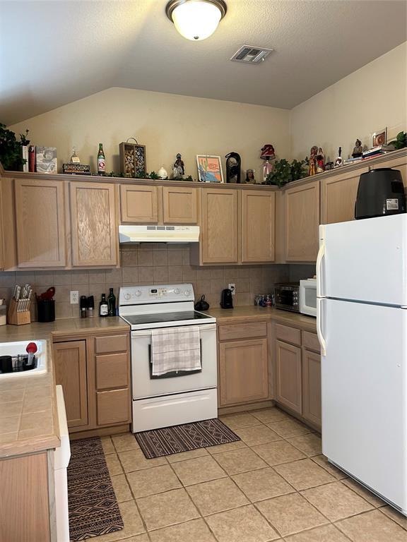 kitchen with under cabinet range hood, visible vents, white appliances, and tasteful backsplash