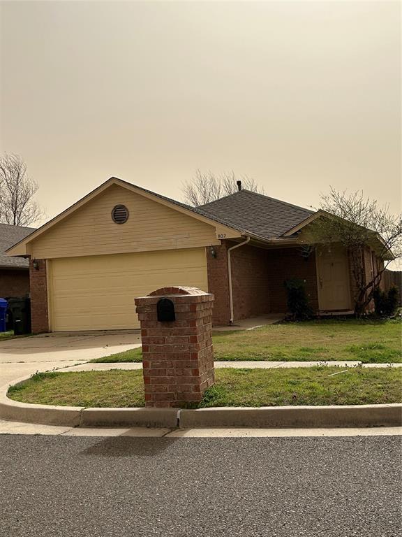 ranch-style house featuring a front lawn, driveway, a shingled roof, a garage, and brick siding
