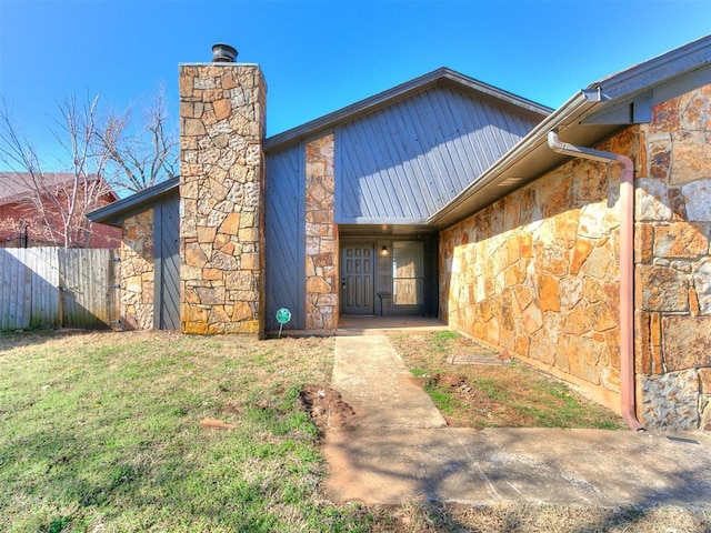 view of exterior entry with stone siding, a chimney, and fence