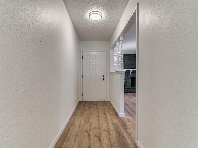 corridor featuring baseboards, a textured ceiling, wood finished floors, and a textured wall