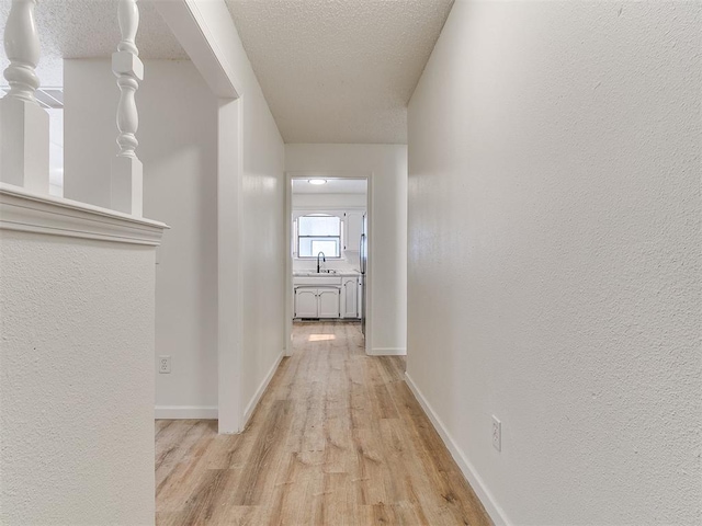 corridor featuring light wood finished floors, a textured ceiling, baseboards, and a sink