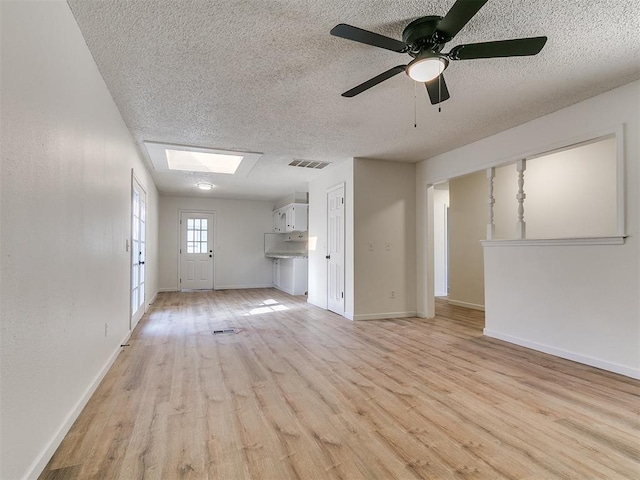 unfurnished living room featuring visible vents, baseboards, a textured ceiling, and light wood-style flooring