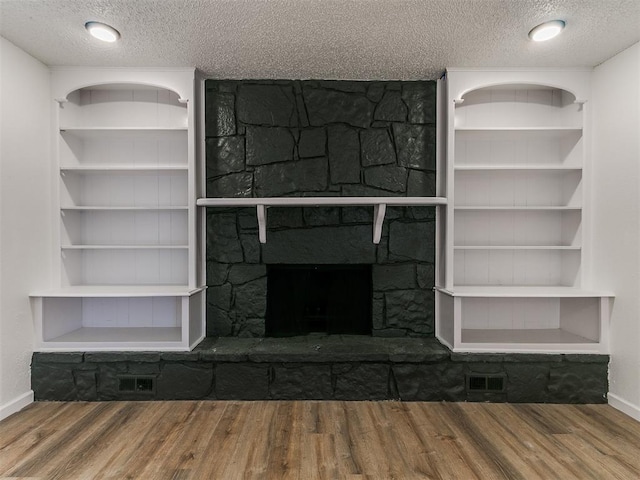 unfurnished living room featuring visible vents, baseboards, a stone fireplace, wood finished floors, and a textured ceiling