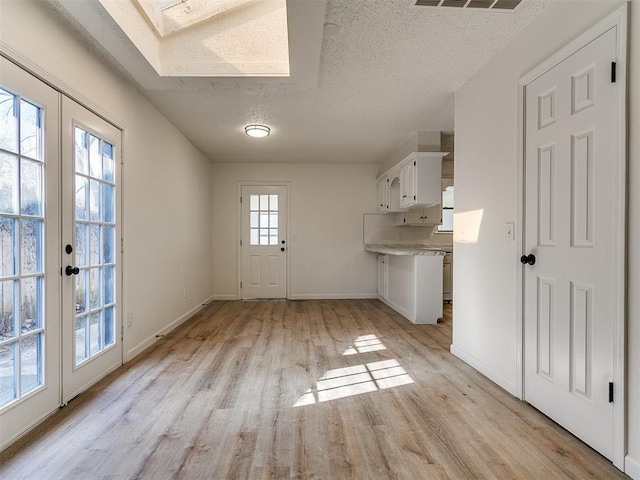 unfurnished dining area featuring baseboards, light wood-style floors, a skylight, and a textured ceiling