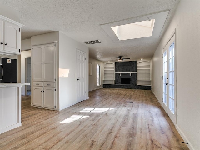 unfurnished living room with light wood-type flooring, a fireplace, visible vents, and a textured ceiling