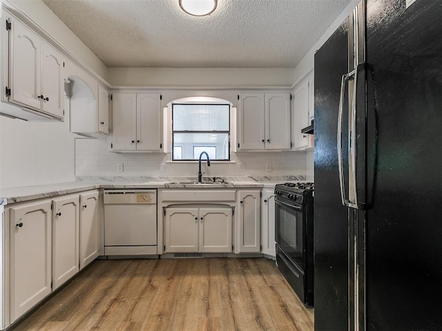 kitchen with a sink, black appliances, white cabinetry, light wood-type flooring, and backsplash