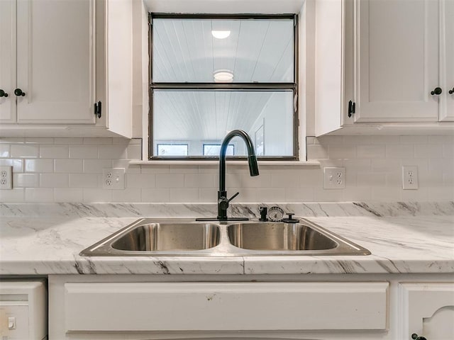 kitchen with backsplash, white cabinets, light stone countertops, and a sink