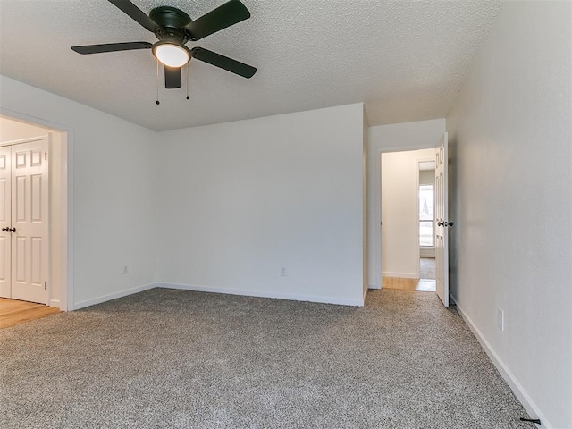 spare room featuring baseboards, light colored carpet, a ceiling fan, and a textured ceiling