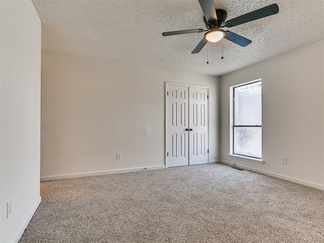 carpeted empty room featuring baseboards, a textured ceiling, and a ceiling fan