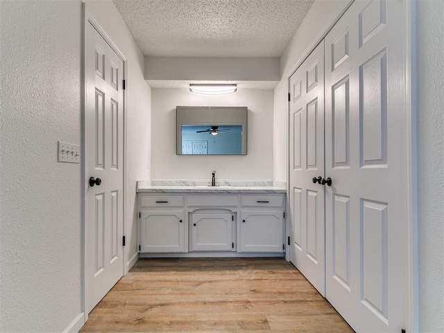 bathroom with a textured ceiling, wood finished floors, ceiling fan, vanity, and a textured wall