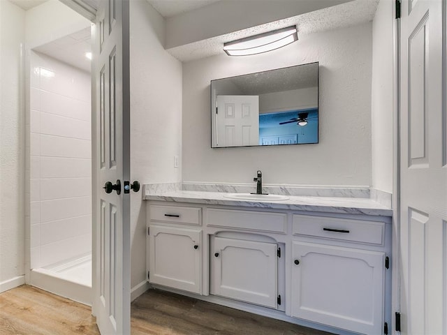 full bathroom featuring ceiling fan, tiled shower, wood finished floors, and vanity