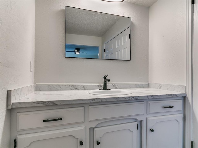 bathroom with a textured ceiling, vanity, a ceiling fan, and a textured wall