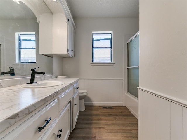 full bathroom featuring toilet, wood finished floors, plenty of natural light, and wainscoting