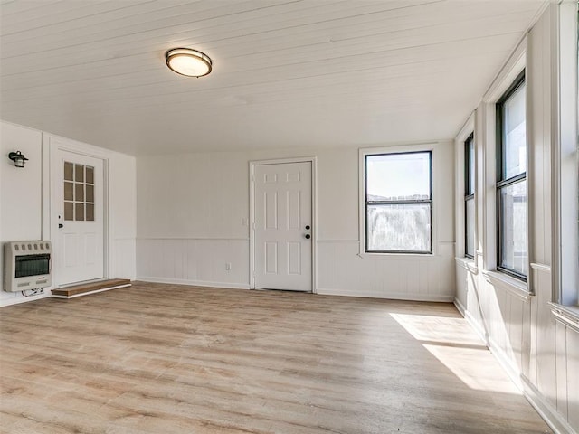 interior space with light wood-style flooring, heating unit, and wainscoting