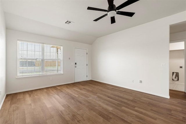 empty room with visible vents, a ceiling fan, wood finished floors, baseboards, and vaulted ceiling