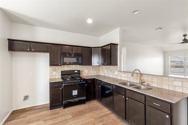 kitchen featuring light stone countertops, dark brown cabinetry, a peninsula, black appliances, and a sink