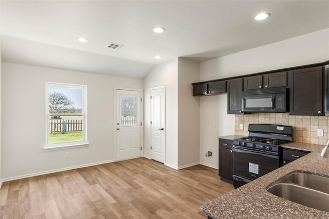 kitchen featuring visible vents, black appliances, dark stone countertops, a sink, and tasteful backsplash