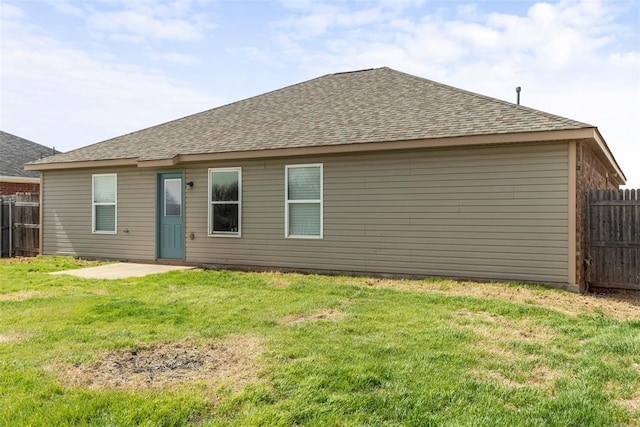 rear view of property with fence, a lawn, and a shingled roof