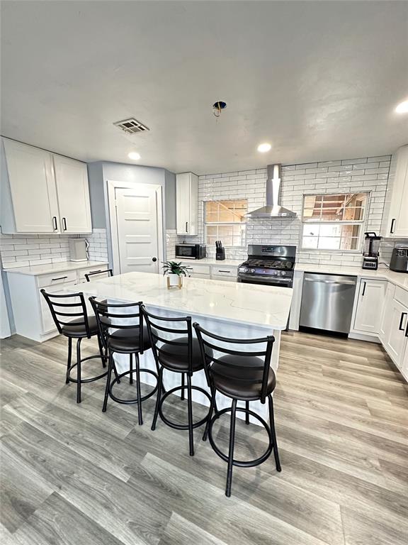 kitchen featuring visible vents, decorative backsplash, light wood-style floors, stainless steel appliances, and wall chimney exhaust hood