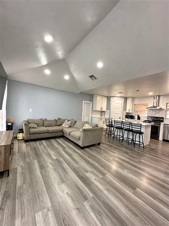 living room with lofted ceiling, recessed lighting, wood finished floors, and visible vents