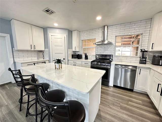 kitchen with visible vents, a breakfast bar area, appliances with stainless steel finishes, dark wood-style floors, and wall chimney exhaust hood