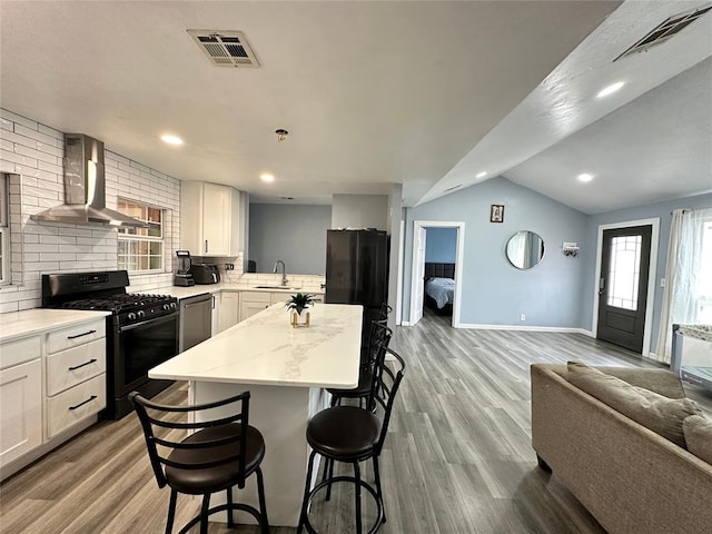 kitchen featuring visible vents, a sink, black appliances, wall chimney exhaust hood, and open floor plan