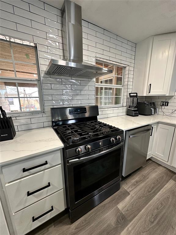 kitchen featuring backsplash, wall chimney range hood, dark wood-style floors, white cabinets, and stainless steel appliances