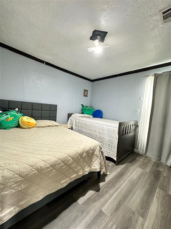 bedroom featuring crown molding, wood finished floors, visible vents, and a textured ceiling