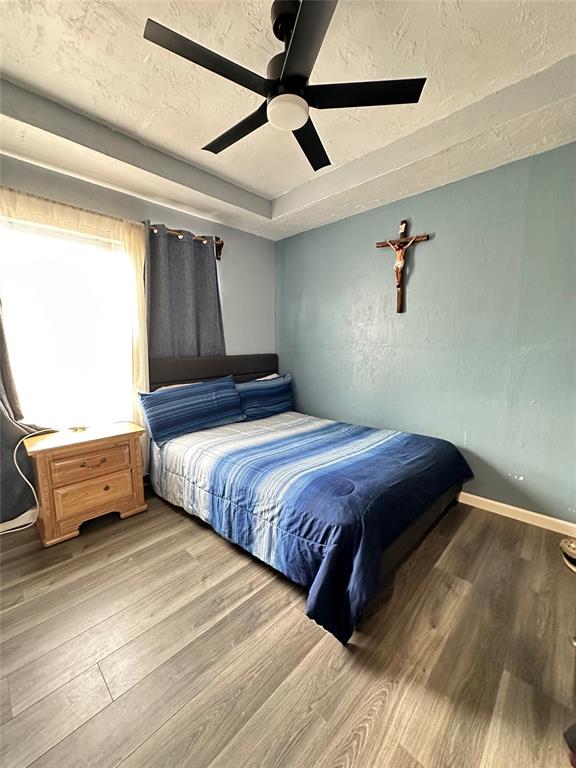 bedroom with baseboards, ceiling fan, wood finished floors, a textured ceiling, and a raised ceiling