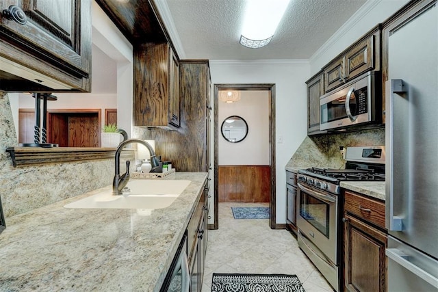 kitchen with a sink, ornamental molding, stainless steel appliances, dark brown cabinets, and a textured ceiling