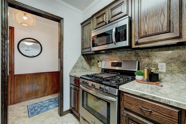 kitchen with wooden walls, dark brown cabinets, a wainscoted wall, ornamental molding, and appliances with stainless steel finishes