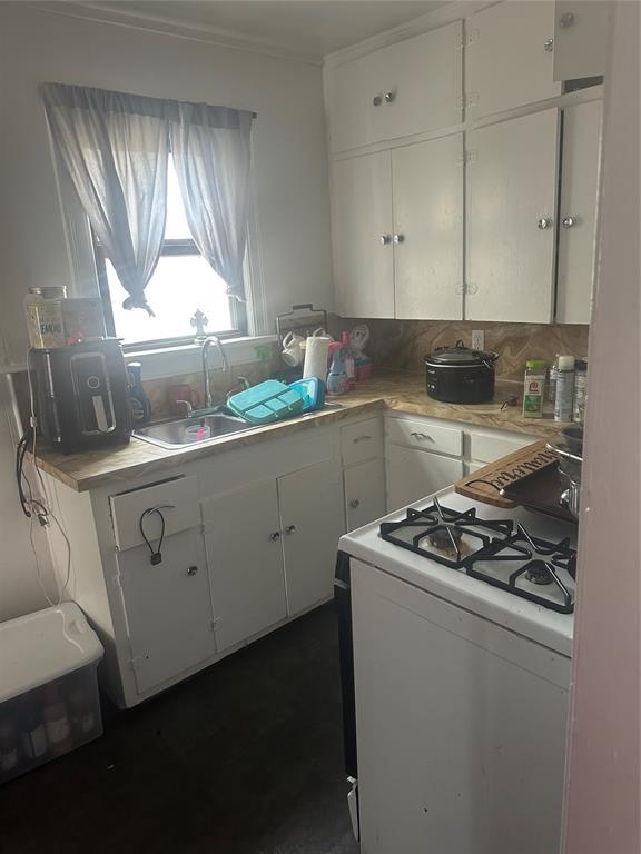 118 NE 2nd St, Moore, OK 73160 - kitchen featuring gas range gas stove, a sink, light countertops, white cabinetry, and ornamental molding