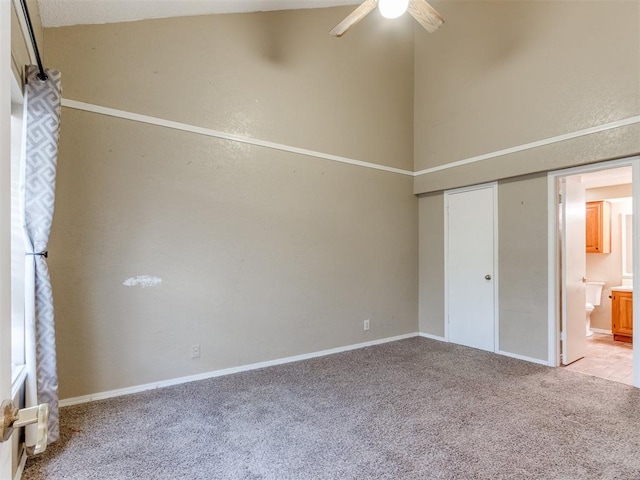 unfurnished bedroom with a ceiling fan, connected bathroom, a closet, carpet, and a high ceiling