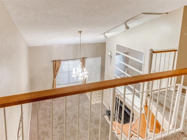 stairs with a textured ceiling, a chandelier, and rail lighting