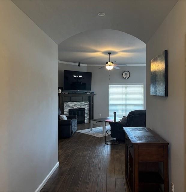 living area featuring a fireplace, dark wood finished floors, baseboards, arched walkways, and ceiling fan