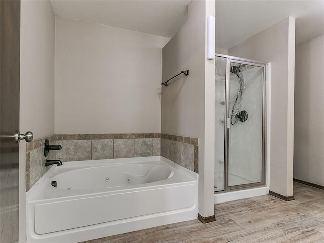 bathroom with baseboards, a tub with jets, wood finished floors, and a shower stall